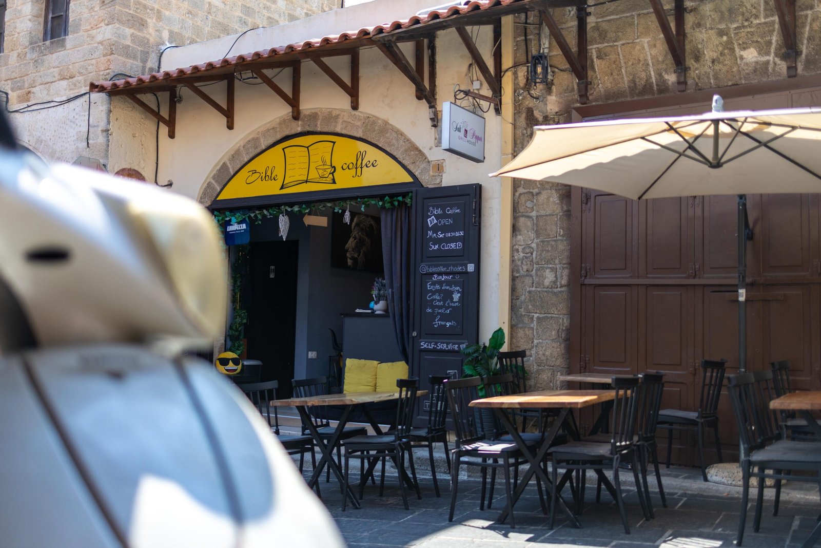 Outdoor seating at Bible Coffee with a scooter parked in the foreground on a street in Rhodes Old Town