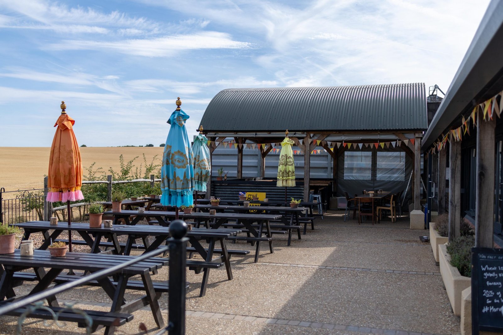 Outdoor courtyard seating at The Mixing Shed Cafe overlooking a wheat field, with covered barn seating and colourful parasols