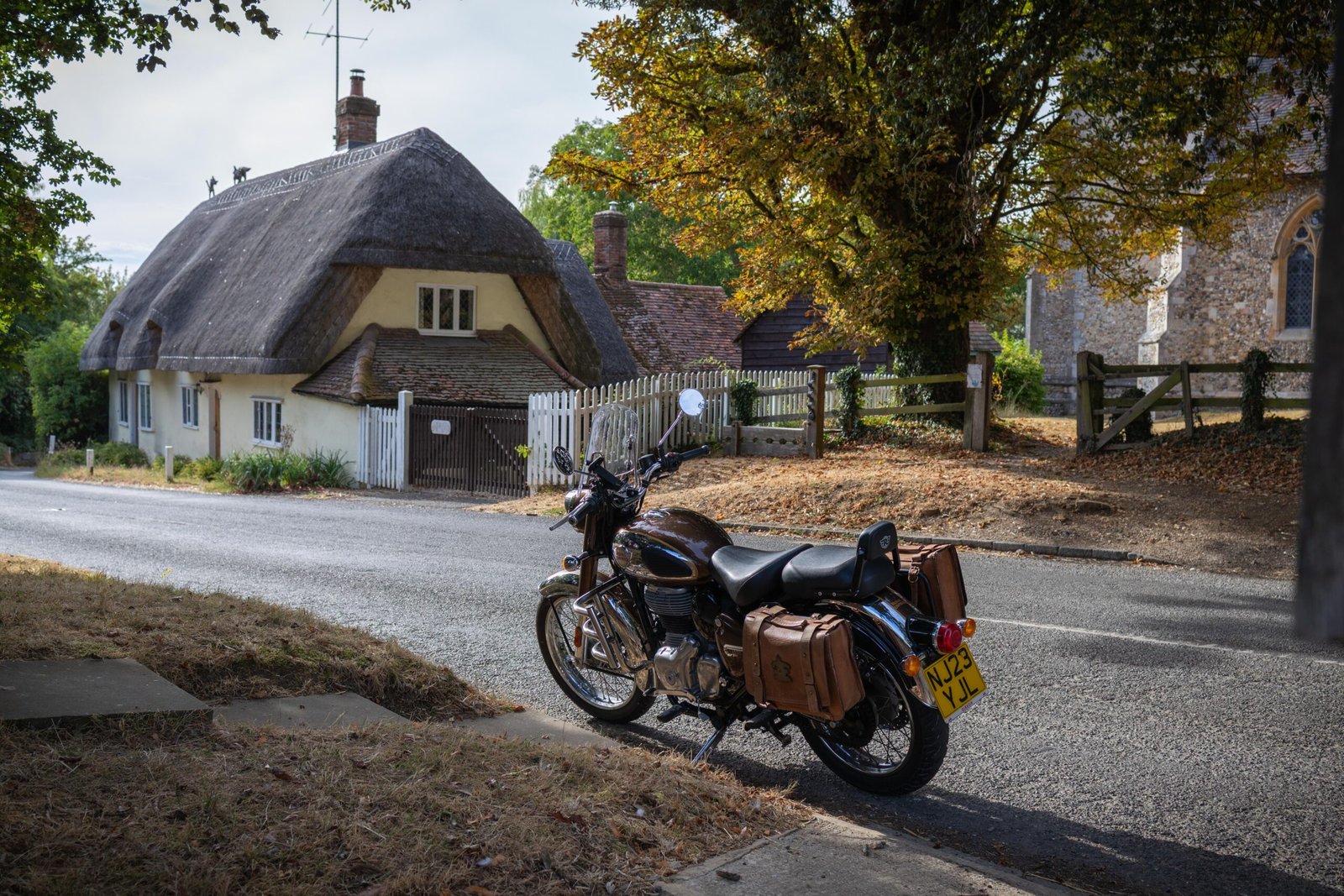A Royal Enfield motorcycle parked in a village with a thatched cottage and church on the ride to The Mixing Shed Cafe