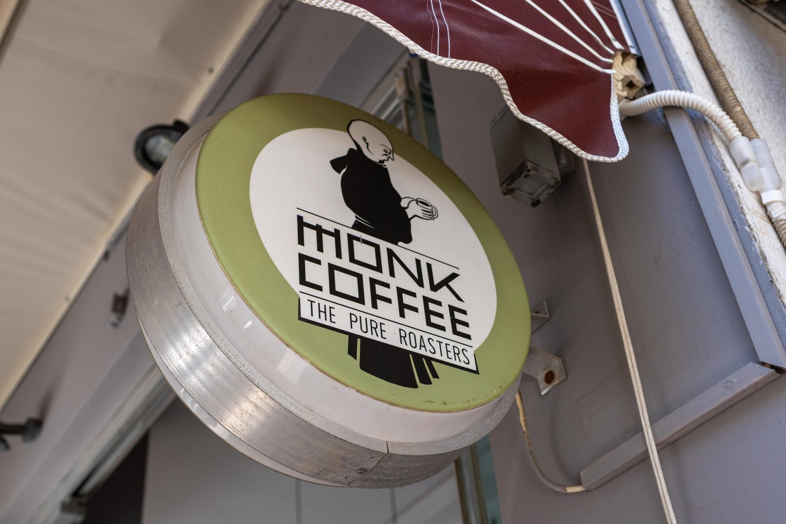 The round hanging Monk Coffee/The Pure Roasters shop sign mounted outside, next to a red awning