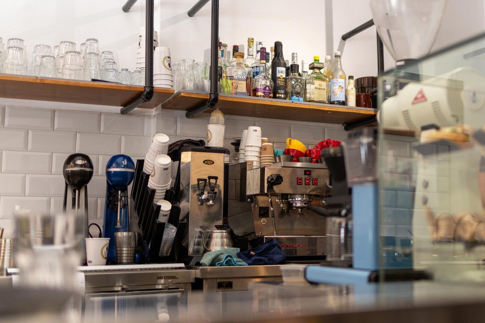 Behind the counter at Monk Coffee/The Pure Roasters, with the espresso machine and stacked cups against white subway tile