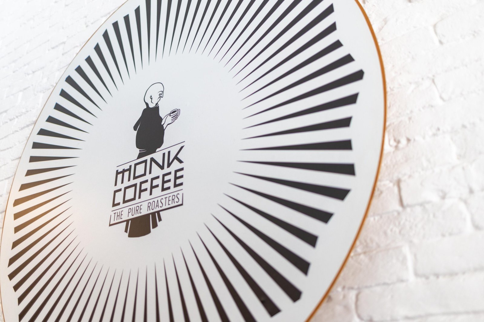 Close-up of the Monk Coffee/The Pure Roasters sunburst logo on white brick
