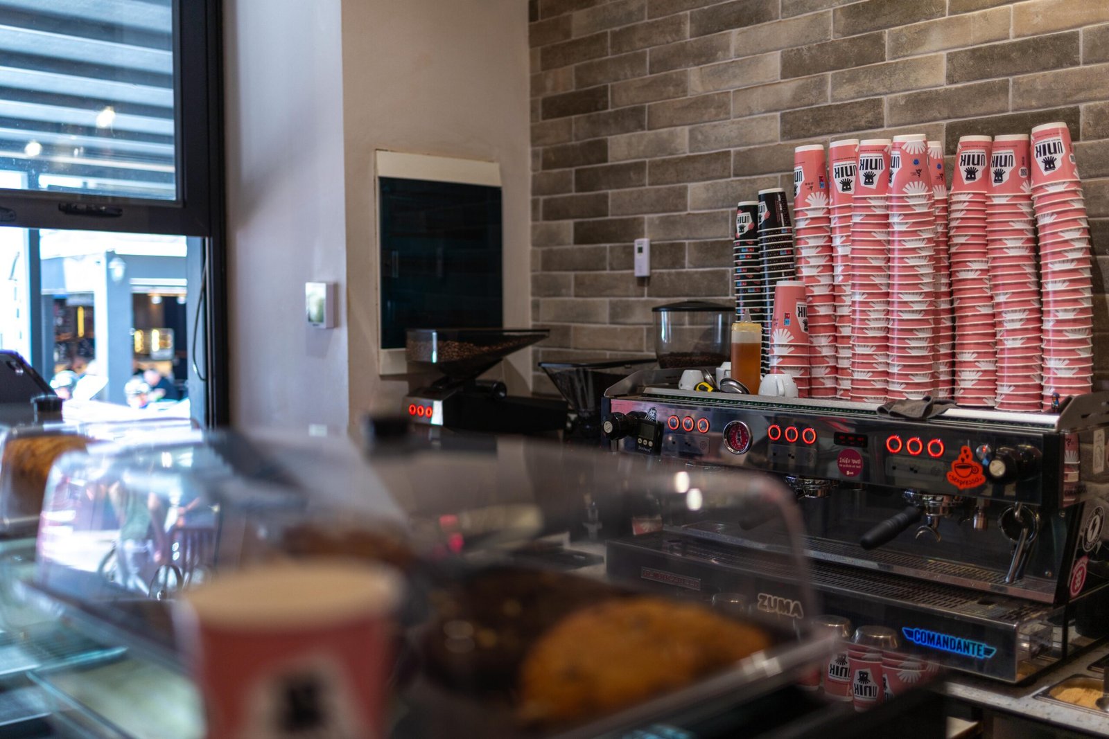 Behind the counter at Unik, stacked branded cups, espresso machine, and pastries in the display case