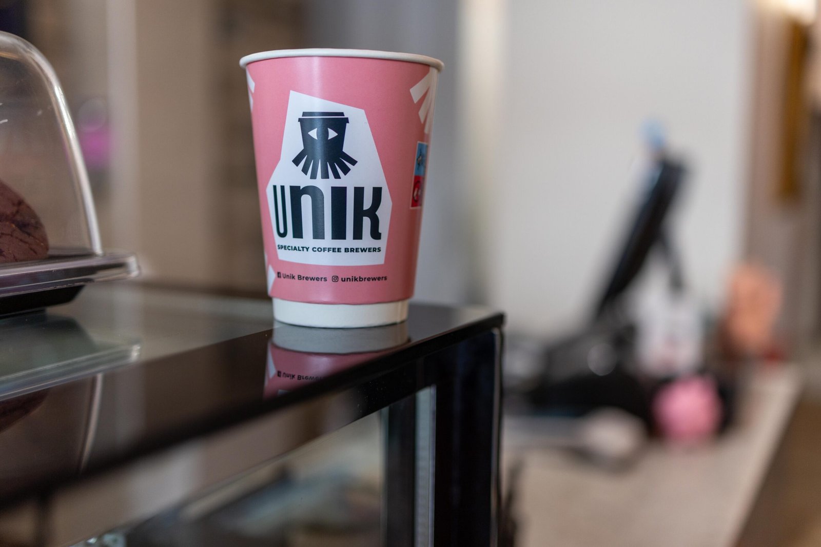 Close-up of a pink Unik Specialty Coffee Brewers branded cup with the squid logo and Instagram handle