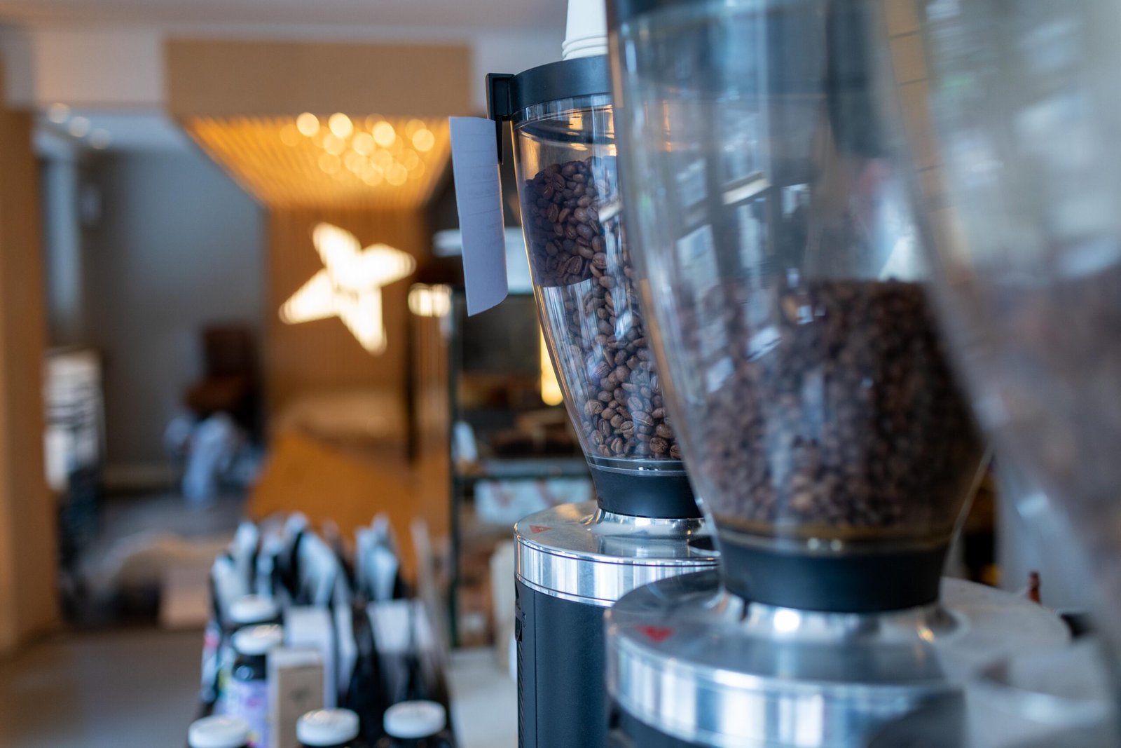 Coffee grinder hoppers in close-up at Velasquez and Van Wezel, with the retail shelf and a star-shaped light fixture blurred behind