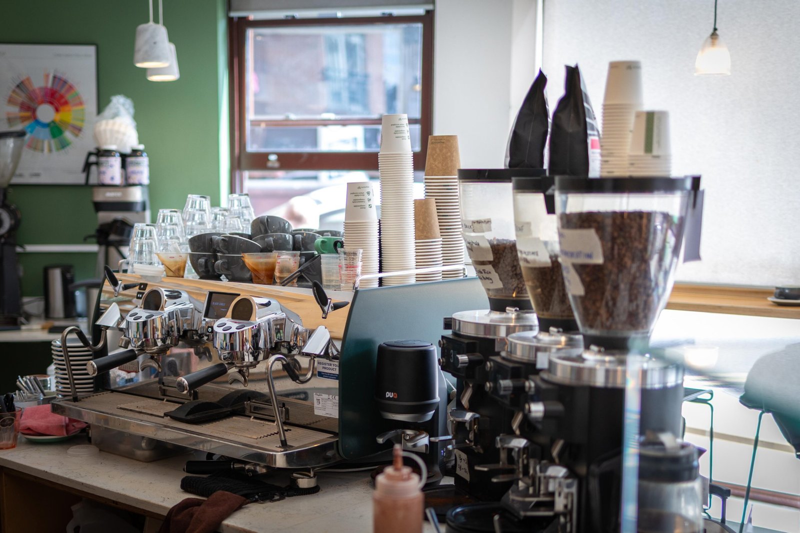 The espresso bar at Velasquez and Van Wezel, with stacked cups, grinders, and a green wall behind the counter