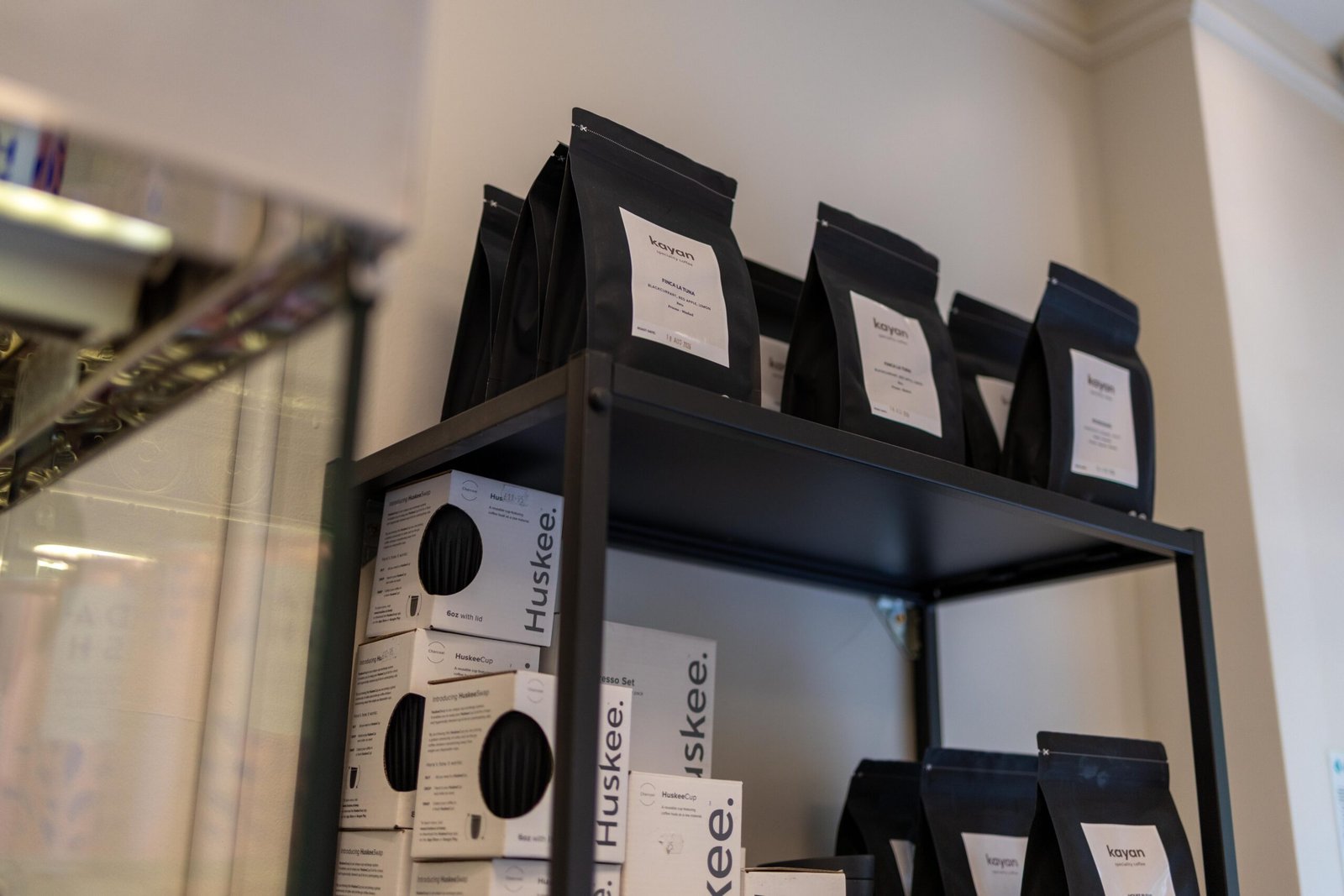 Kayan's own retail coffee bags on a shelf alongside Huskee reusable cup boxes