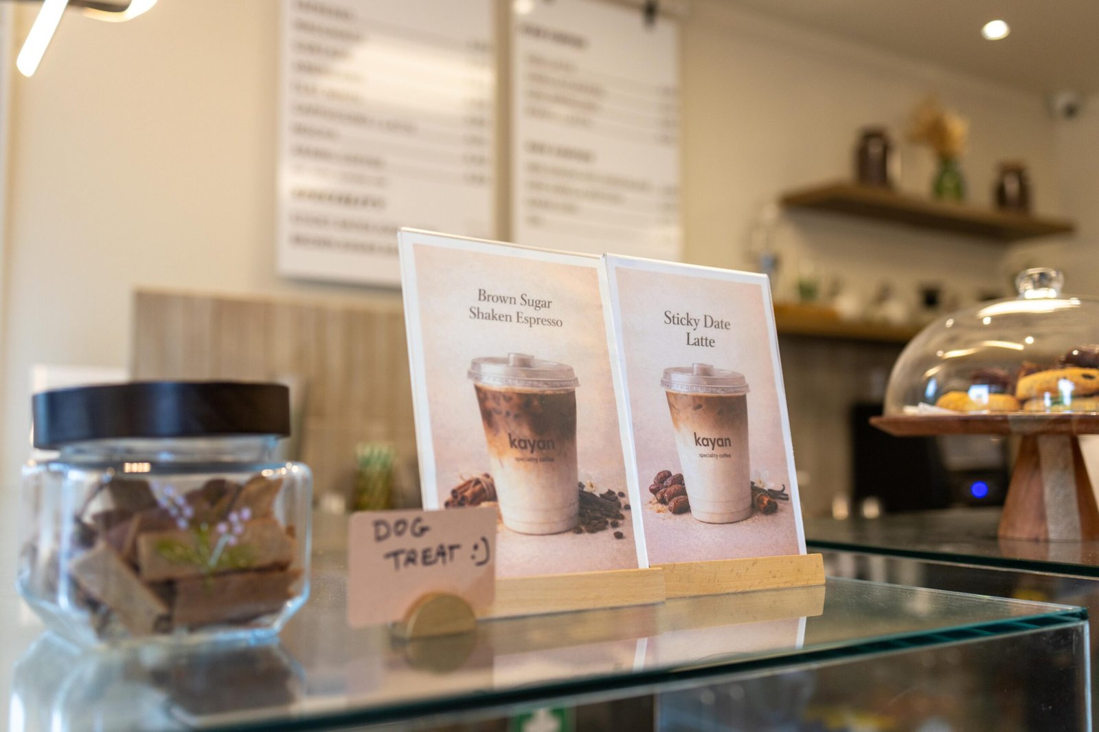 A Sticky Date Latte promotional card on the counter at Kayan Specialty Coffee, next to a jar of dog treats