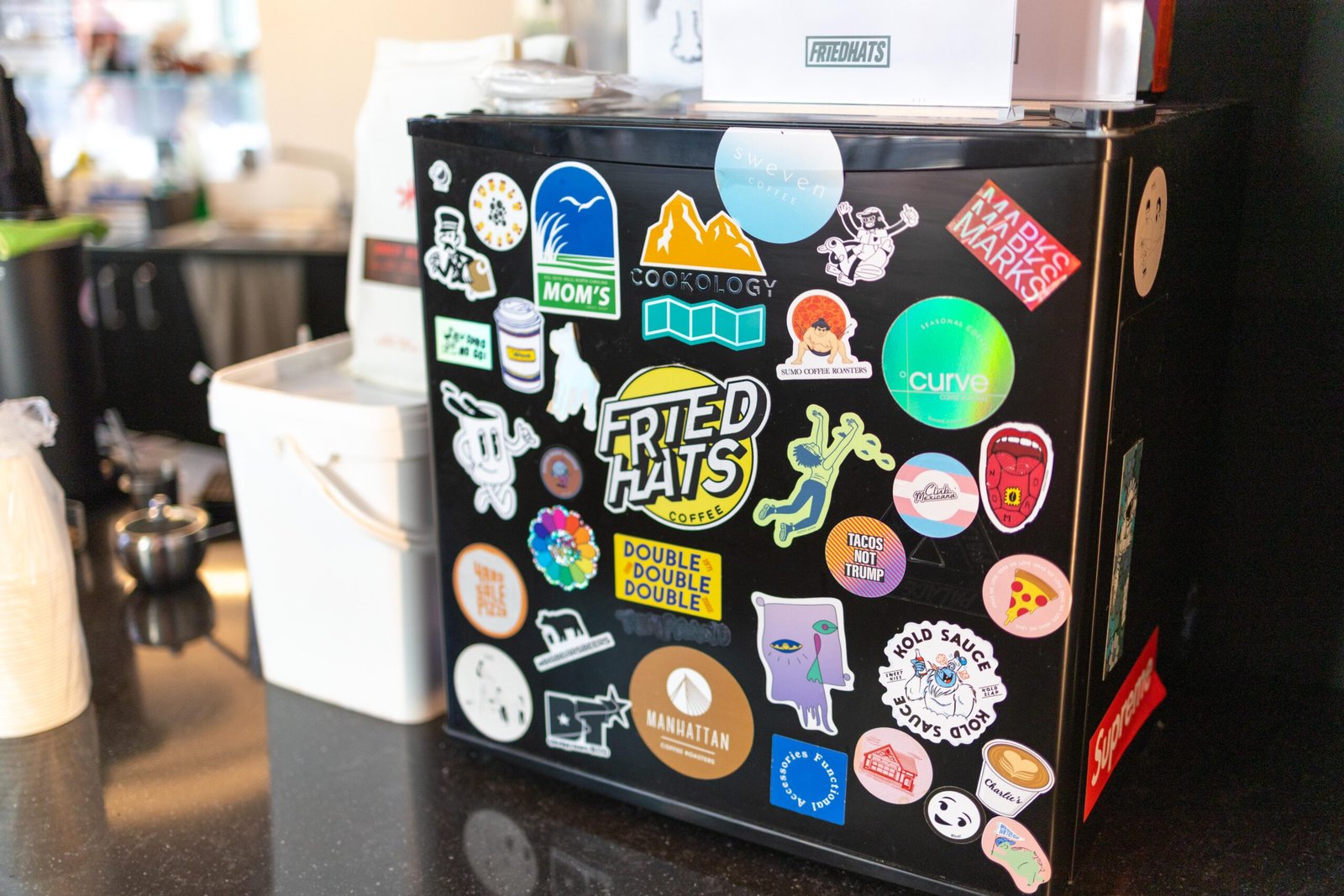 A fridge covered in stickers behind the counter, including a Friedhats Coffee sticker