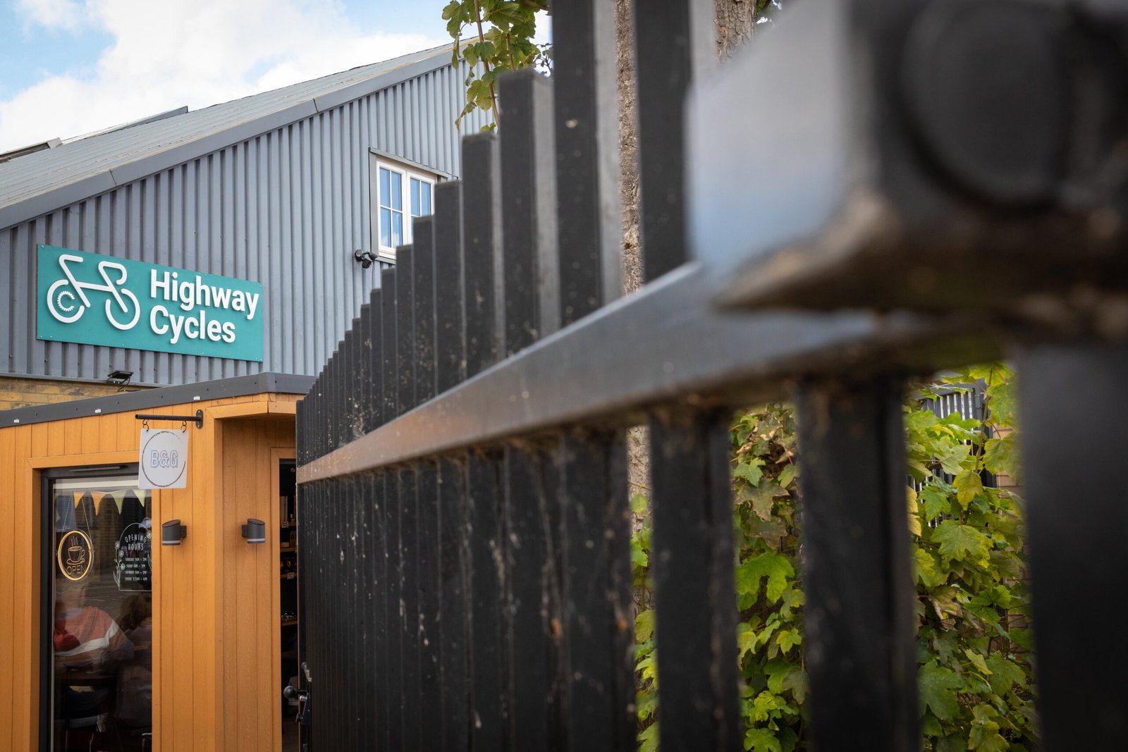 The wooden kiosk of Bean & Gone Coffee seen through railings beside Highway Cycles