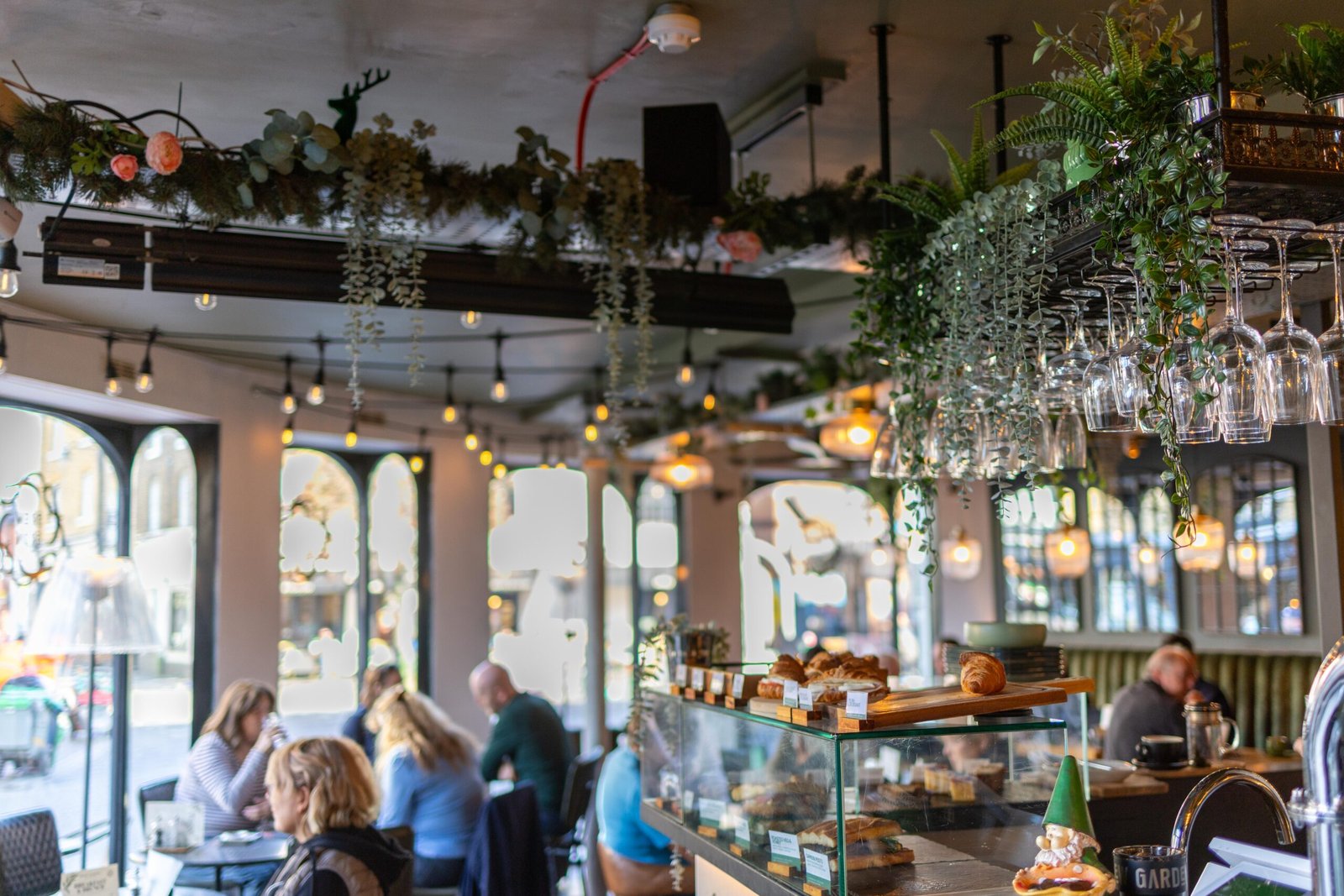Customers seated beneath hanging plants and arched windows inside Brew Garden