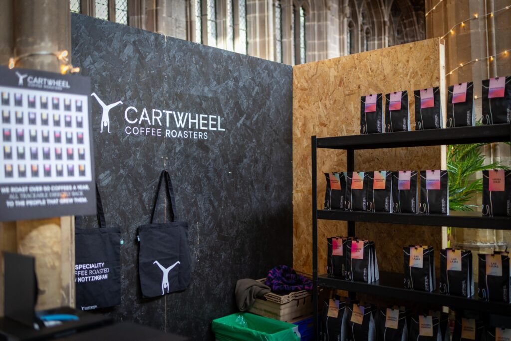 The Cartwheel Coffee Roasters stand with its logo on a dark wall and shelves of coffee bags