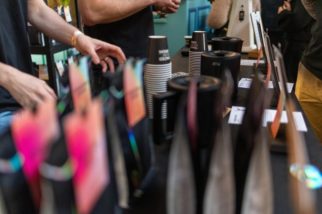 Hands reaching across the Cartwheel counter, with paper cups, brewers and colourful bag tags in the foreground