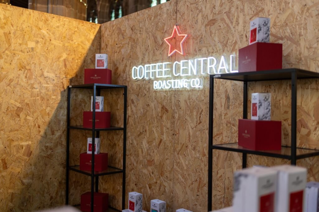 The Coffee Central Roasting Co neon sign on a wooden board, with red boxes and coffee packs on black shelves