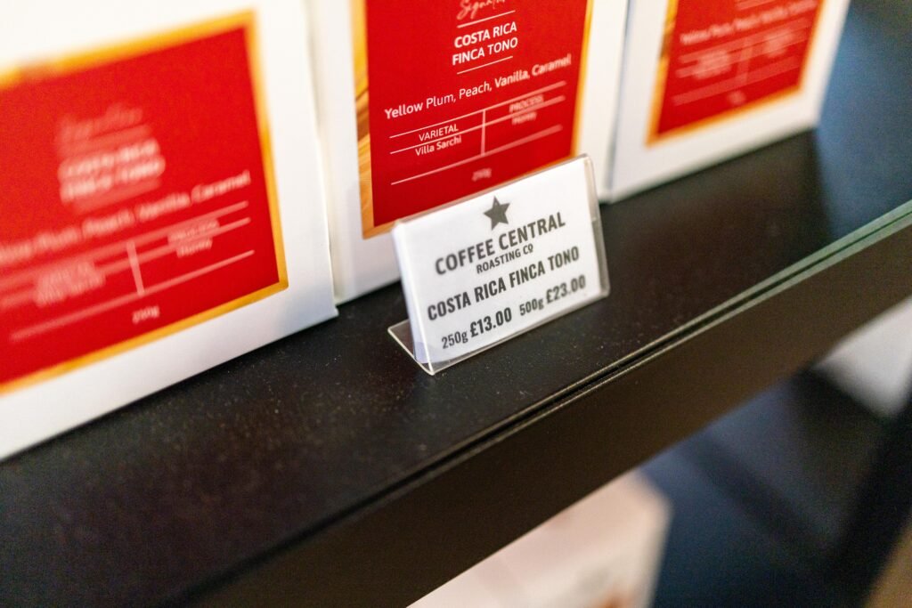 A shelf label for Costa Rica Finca Tono coffee in front of red Coffee Central packs