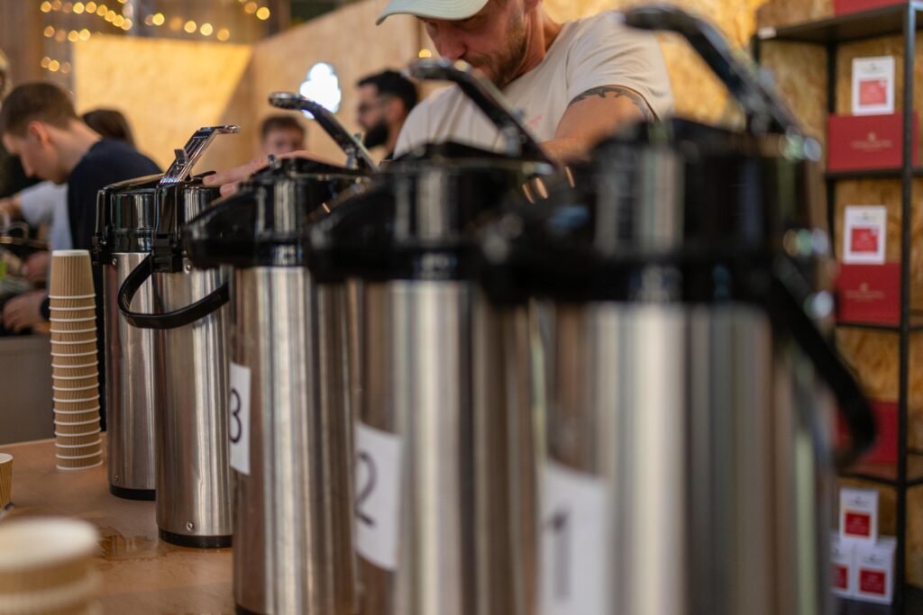 A row of numbered steel airpot flasks on the Coffee Central Roasting Co stand, with a team member behind
