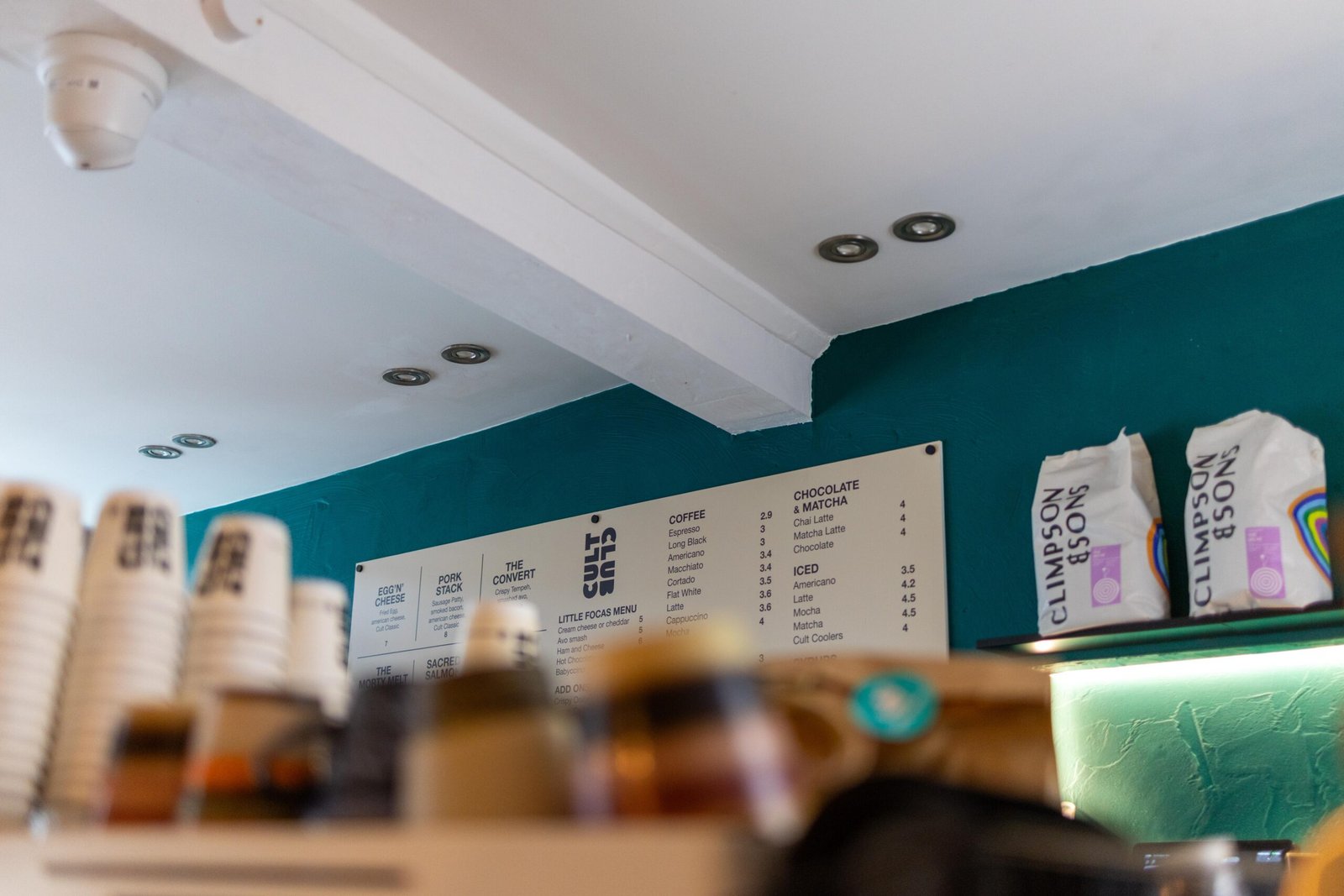 Takeaway cups, menu board and coffee bags on the counter at Cult Club Coffee