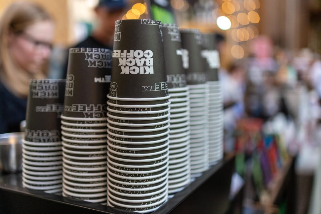 Stacks of Kickback Coffee paper cups on the counter, with festival visitors blurred behind