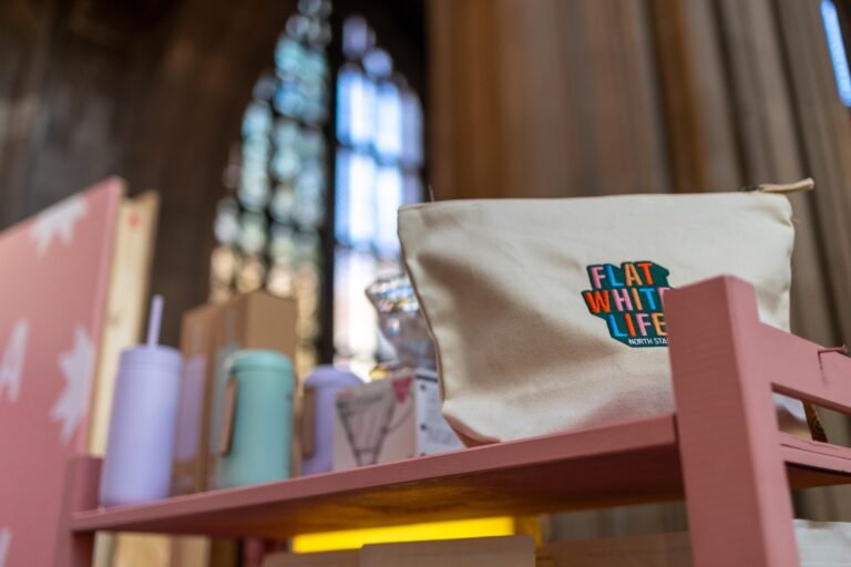 A Flat White Life pouch from North Star Coffee on a pink shelf, with a stained glass church window behind