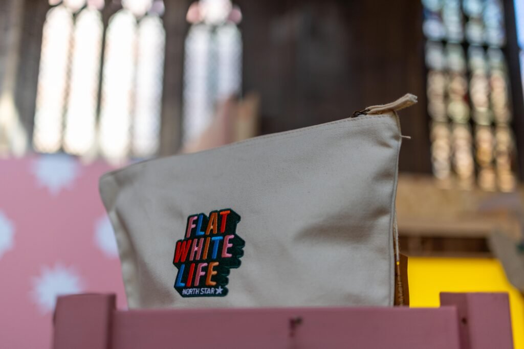 A Flat White Life pouch from North Star Coffee on a pink shelf, with church windows behind