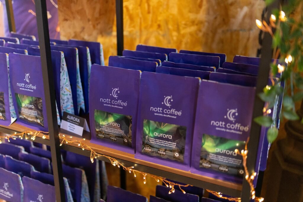 Rows of purple Nott Coffee Aurora decaf bags on a shelf wrapped in fairy lights