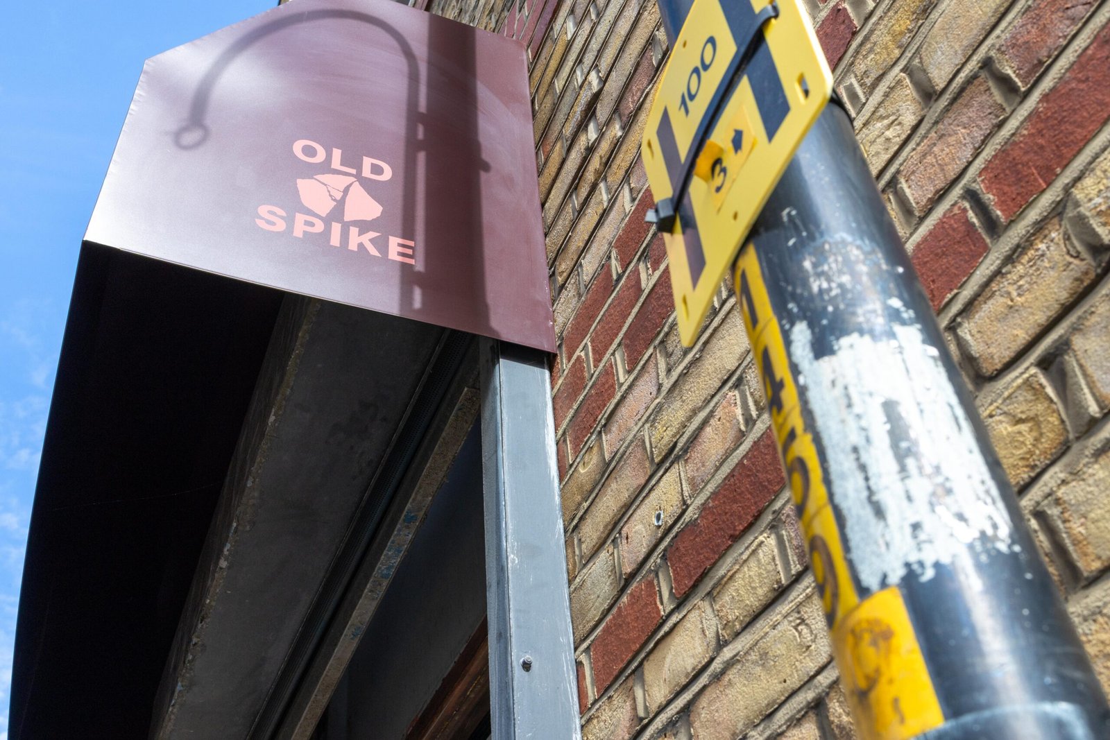 Old Spike hanging sign against a brick wall and blue sky in Southwark