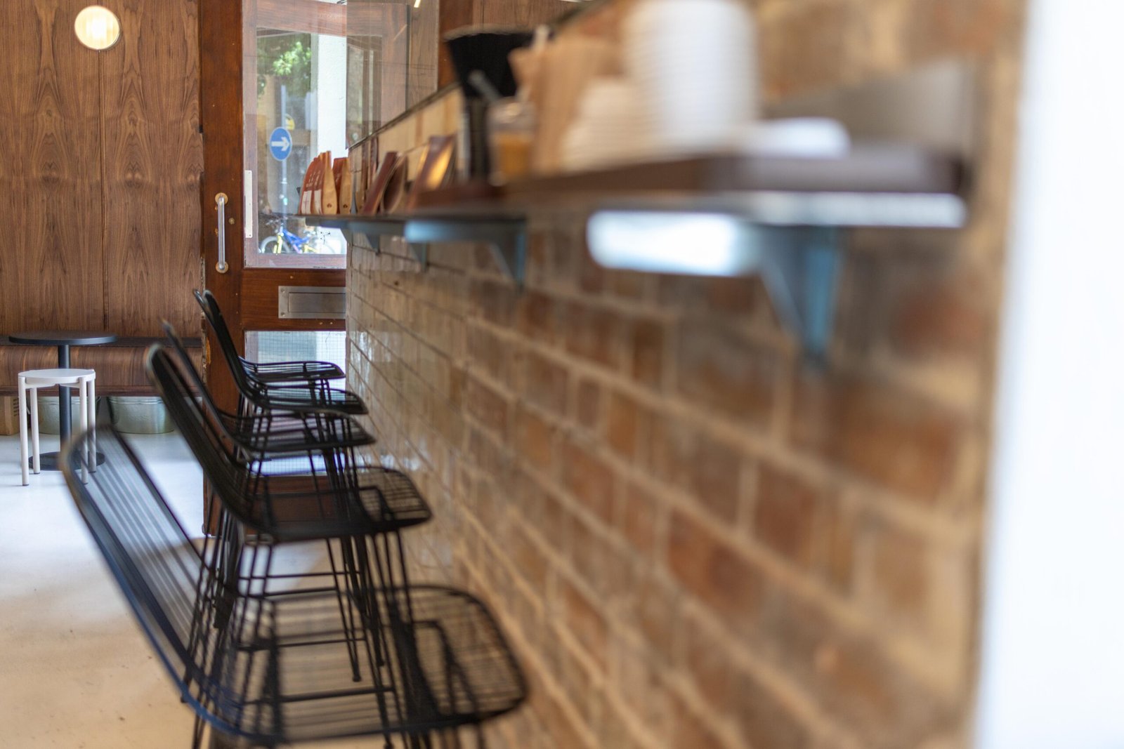 Black wire bar stools along an exposed brick wall with a wooden shelf