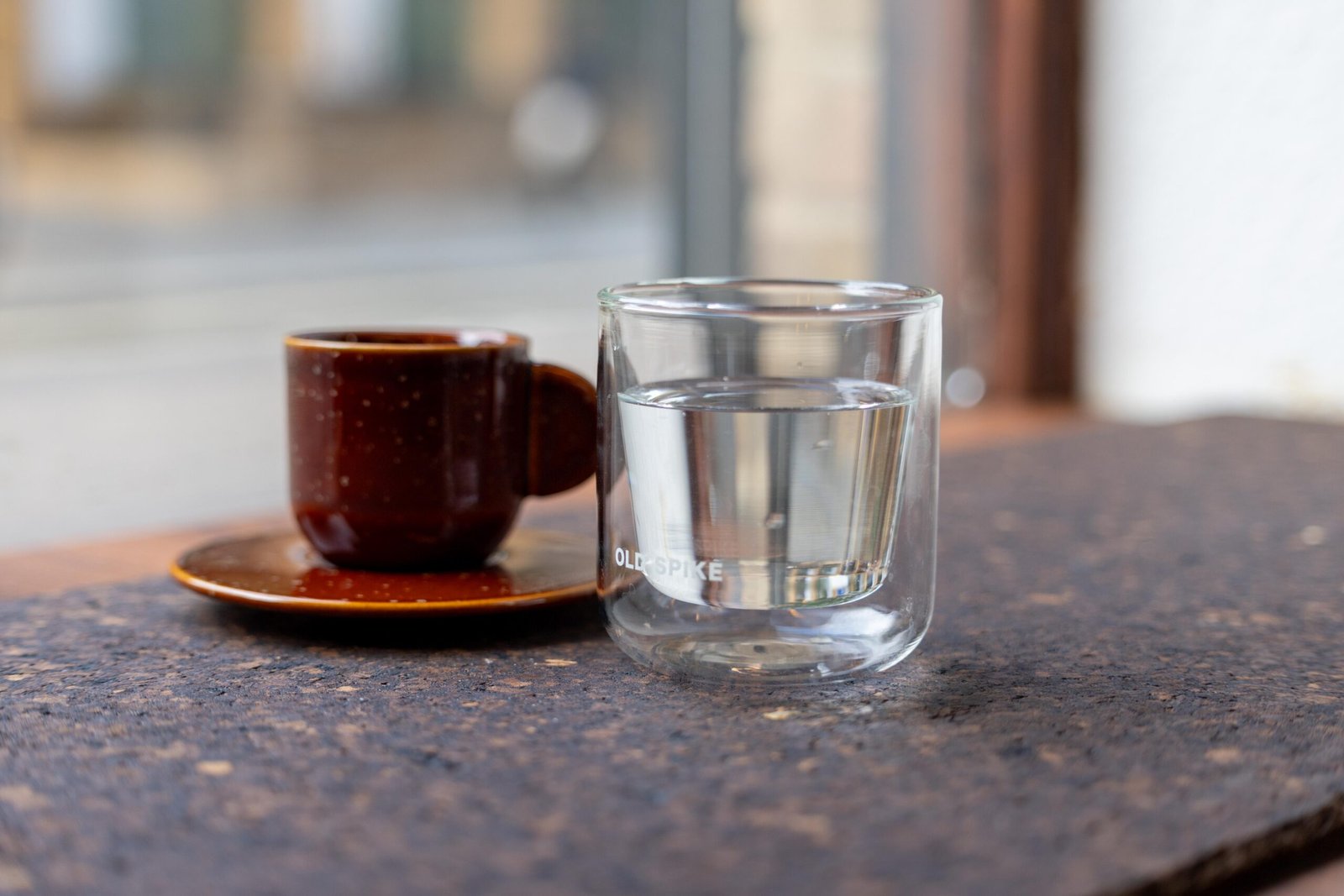 An espresso in a brown cup and saucer beside a glass of water on the counter