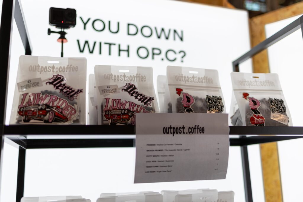 Outpost Coffee bags on a black shelf beneath a You down with OPC sign