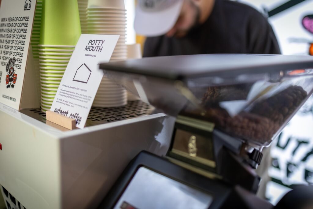 Coffee grinder hopper and paper cups at the Outpost Coffee stand beside a Potty Mouth coffee card