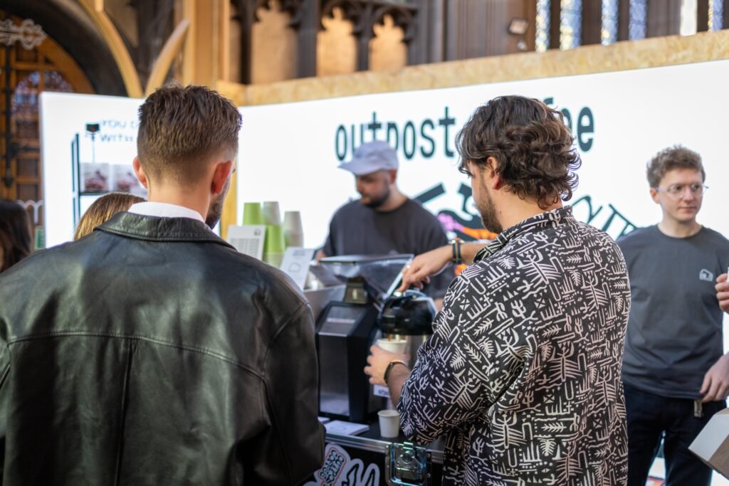 Visitors gathered at the Outpost Coffee stand beneath the church roof, one pouring a coffee from a flask