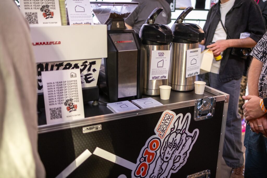 Outpost Coffee brew station on a black flight case with flasks, tasting cups and stickers