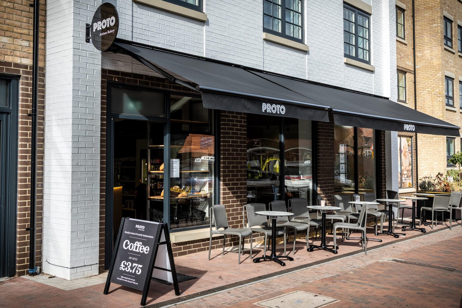 Outdoor tables and a coffee sign outside Proto Artisan Bakery in Hertford