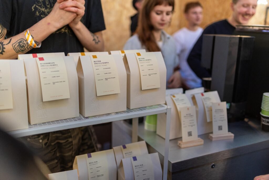 Cream paper bags of Saints of Mokha coffee on a shelf, with customers waiting behind