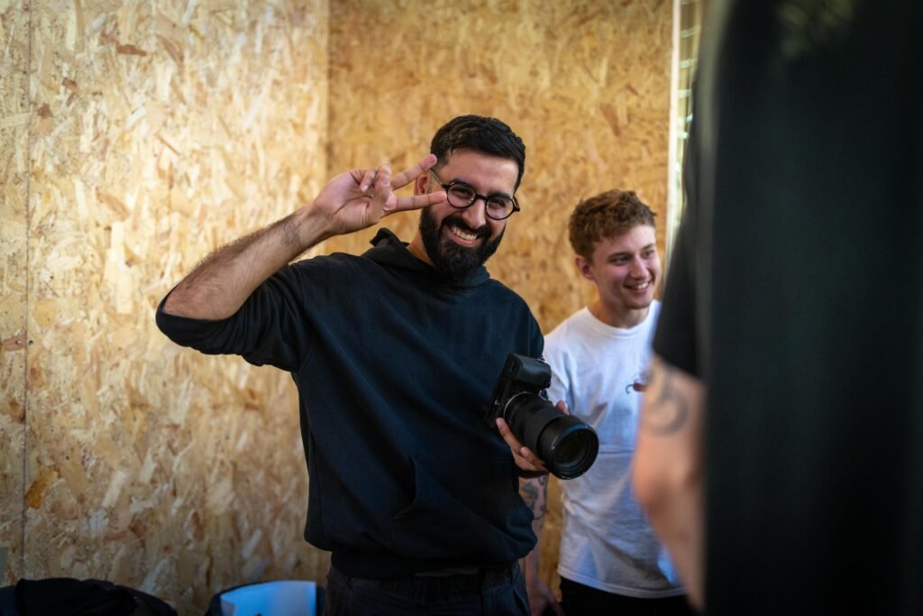 A smiling Saints of Mokha team member holding a camera and making a peace sign at the stand
