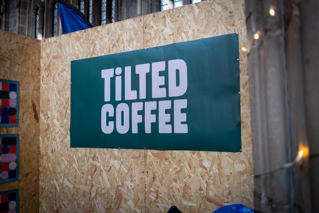 Green Tilted Coffee sign on a wooden board at the Tilted Coffee stand